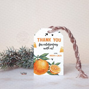 May include: A white gift tag with orange and green watercolor illustrations of oranges and leaves. The tag reads "THANK YOU for celebrating with us!" with the names "Anisha & Jacob" below. A brown string is attached.