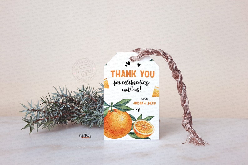May include: A white gift tag with orange and green watercolor illustrations of oranges and leaves. The tag reads "THANK YOU for celebrating with us!" with the names "Anisha & Jacob" below. A brown string is attached.