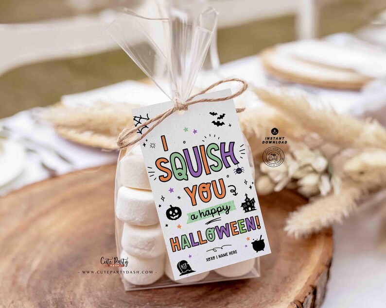 May include: A clear cellophane bag tied with twine, filled with marshmallows and a Halloween-themed tag. The tag reads "I SQUISH YOU a happy HALLOWEEN!" with colorful graphics of a pumpkin, spider, and haunted house. The bag sits on a wooden surface.