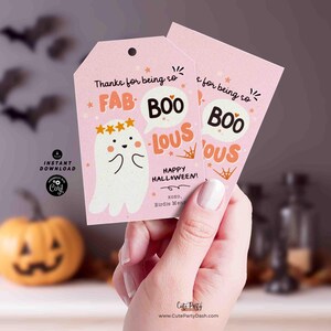 May include: Pink Halloween gift tags with a ghost illustration and the words "FAB BOO LOUS". The tags also say "Happy Halloween!" and include the text "Thanks for being so". The tags are held by a person.