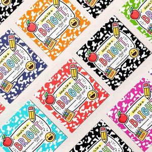 Op de afbeelding: Een verzameling kleurrijke vierkante stickers met een schoolthema. Elke sticker bevat de tekst "Here's to a BRIGHT school year!" samen met illustraties van een appel, potlood, kleurpotloden en een smiley. De achtergrond van elke sticker heeft een andere kleur.