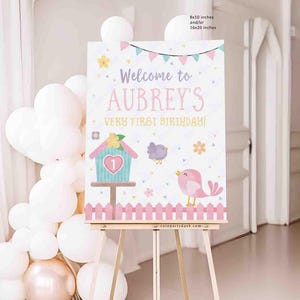 May include: A welcome sign for a birthday party, featuring the text "Welcome to Aubrey's Very First Birthday!" in pink and pastel colors. The sign includes illustrations of a birdhouse, birds, and flowers. The sign is 8x10 inches or 16x20 inches.