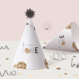 Peut inclure: Chapeau de f&ecirc;te imprimable avec un motif de cookie et le texte "So much fun to be one". Le chapeau est blanc avec des illustrations de cookies marrons et noirs. Le chapeau est pos&eacute; sur une surface blanche avec des confettis.