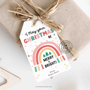 May include: A white gift tag with a rainbow, Christmas trees, and the text "May your Christmas be Merry & Bright!"  From. Name Here. -CUTEPARTYDASH.COM-