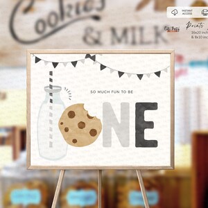 May include: A printable sign for a first birthday party featuring a milk bottle, a cookie, and the word "ONE" in black, grey, and white. The text "So much fun to be" is above the number one. The sign is on an easel.