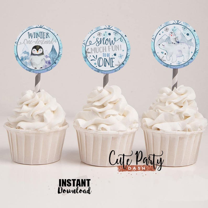 May include: Three cupcake toppers with winter themes. The first topper features a penguin with the text "Winter One-derland". The second topper features snowflakes and the text "Snow Much Fun! To Be One". The third topper features a polar bear and a penguin with a mountain scene in the background.