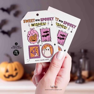 Pu&ograve; includere: Due etichette regalo a tema Halloween con la scritta "Sweet and Spooky Wishes!" e illustrazioni di zucca, pipistrelli e un fantasma. Le etichette sono tenute in mano.