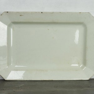 May include: A white rectangular serving platter with slightly rounded edges. The platter is made of ceramic and has a smooth, glossy finish.
