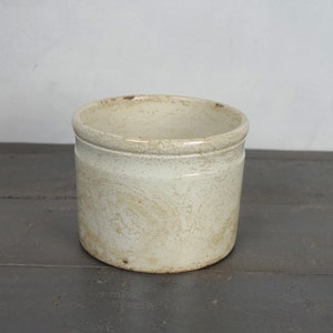 以下が含まれることがあります： わずかにざらざらした表面を持つ白い陶器の壺。壺は丸い形をしていて、開口部が広い。