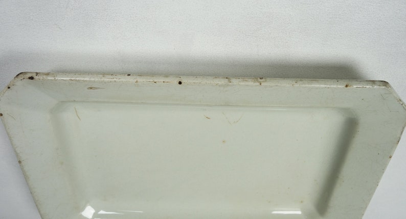 May include: White rectangular serving platter with a slightly raised edge. The platter has a slightly off-white color and shows signs of wear.
