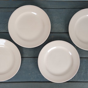 May include: Four plain white ceramic dinner plates on a dark blue wooden surface.