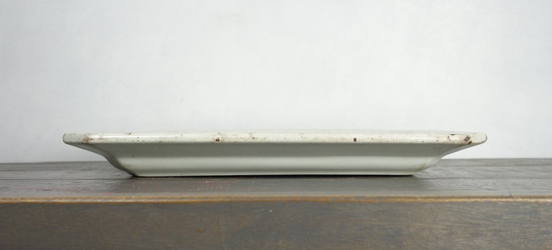 May include: A white rectangular ceramic serving tray with a slightly raised edge. The tray has a rustic, vintage look with subtle brown speckles throughout.