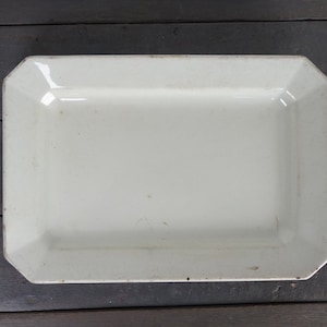 Peut inclure: Un plat de service rectangulaire blanc avec des bords légèrement arrondis. Le plat est en céramique et a une finition lisse et brillante.