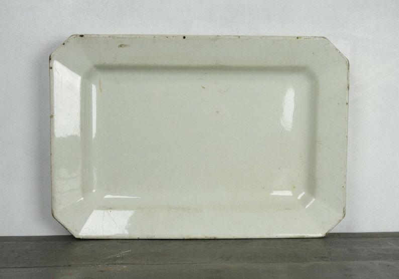May include: A white rectangular serving platter with slightly rounded edges. The platter is made of ceramic and has a smooth, glossy finish.