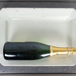 May include: A green glass bottle of champagne with a gold foil top sits in a white rectangular serving dish.