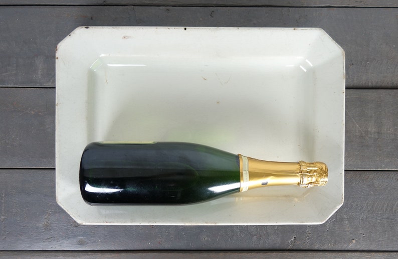 May include: A green glass bottle of champagne with a gold foil top sits in a white rectangular serving dish.
