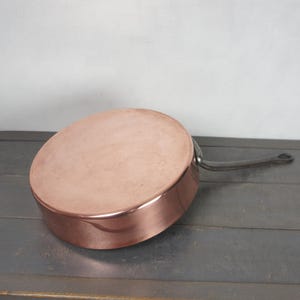 Peut inclure: Une casserole en cuivre avec une longue poignée sombre. La casserole est ronde avec une surface brillante. La poignée est fixée sur le côté. Ustensiles de cuisine.
