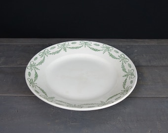 May include: White ceramic plate with a green decorative border of repeating bows and floral designs.