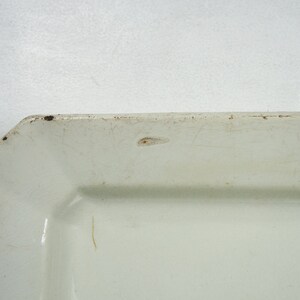 May include: A white rectangular ceramic serving dish with a slightly raised rim. The dish has a slightly off-white color and shows signs of wear and tear.
