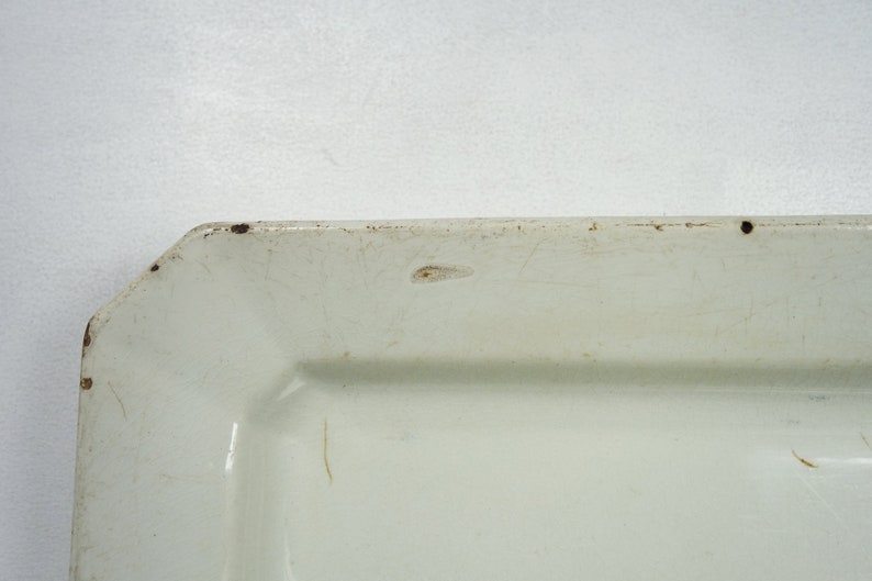 May include: A white rectangular ceramic serving dish with a slightly raised rim. The dish has a slightly off-white color and shows signs of wear and tear.