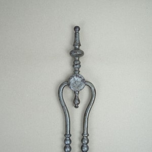 May include: A vintage metal fireplace tool with a decorative finial and a round handle. The tool is made of iron and has a dark gray finish.