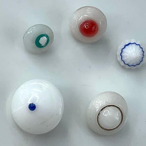May include: A collection of five glass eye cabochons in various designs. One has a red iris, another a blue dot, and a third has a green iris. The other two have a blue outline and a brown outline.