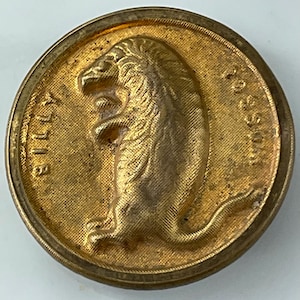 May include: A circular gold-toned metal button featuring a raised relief of a standing creature in profile. The text BILLY is embossed on the left side and the text POSSUM is embossed on the right side of the central figure on a textured background.