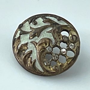 May include: Round antique button with a detailed design. The button features a light green background with ornate gold-colored metal filigree and clear crystal accents. The button's design includes floral and scroll elements.