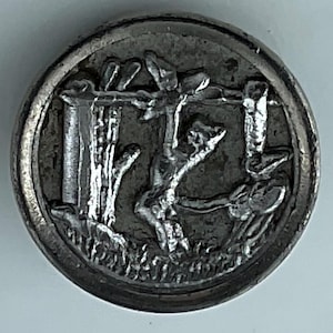 May include: A round, silver-toned button with a detailed relief design. The central image depicts a figure on a cross, flanked by architectural elements and figures. The button has a raised edge and a slightly worn appearance.