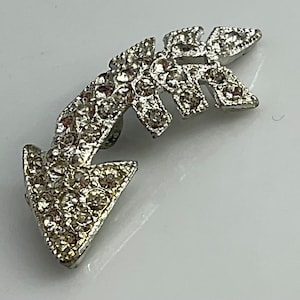 May include: Silver arrow brooch with clear rhinestones. The arrow is curved and has a pointed tip.