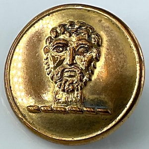 May include: A round, antique brass button with a detailed relief of a bearded man's face. The button has a raised border and a detailed depiction of the man's hair, beard, and facial features. The button is likely vintage and has a worn appearance.