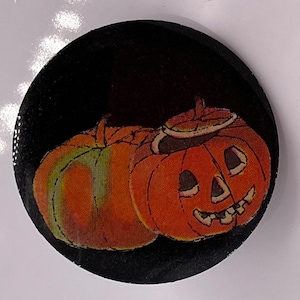 May include: Two orange pumpkins with carved faces on a black background. The pumpkin on top has a stem and a carved smile with teeth. The pumpkin on the bottom is partially obscured by the top pumpkin.