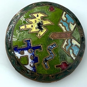 May include: Round, vintage cloisonné button with a green background and colorful geometric designs. The button features yellow, blue, white, and red shapes outlined in gold. The outer edge has a dark green, textured border.
