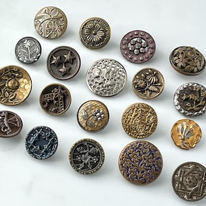 May include: A collection of antique buttons in various sizes and designs. The buttons feature intricate details, including floral patterns, stars, and geometric shapes. Colors range from gold and bronze to silver and blue, showcasing a variety of textures and finishes.