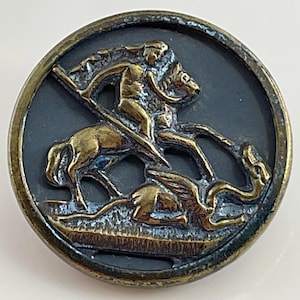 May include: A gold-toned metal button with a raised design of a knight on horseback slaying a dragon. The button has a dark blue background.