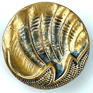 May include: A round, antique-style button with a gold finish and a textured design. The button features a central pattern of stylized feathers with blue accents, and a dotted border. The button is likely made of metal.