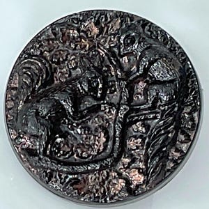 May include: A round, dark gray button with a detailed relief of two squirrels among foliage. The button has a metallic sheen and a textured surface, suggesting an antique or vintage design. The squirrels are depicted in a naturalistic style.