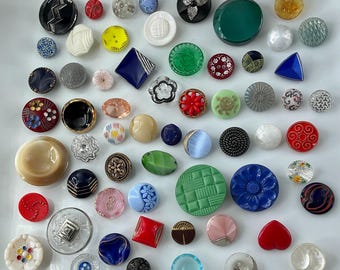 May include: A collection of assorted sewing buttons in various shapes, sizes, and colors, including round, square, and heart-shaped designs. The buttons feature diverse textures, patterns, and materials such as plastic, glass, and metal in shades of red, blue, green, black, white, and gold.