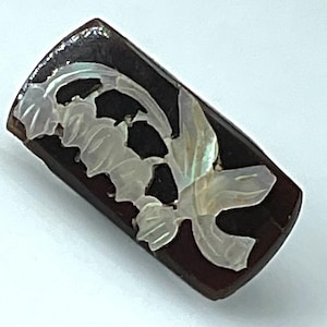 May include: A rectangular, dark brown decorative object with a carved, iridescent white floral design. The floral design appears to be made of mother-of-pearl. The object has a slightly curved top edge.