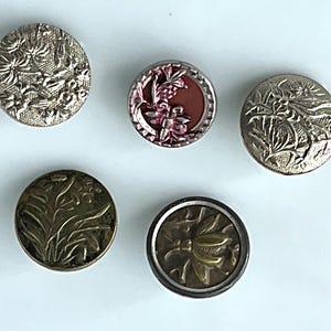 May include: Five vintage buttons with floral and insect designs. The buttons are in various colors, including silver, gold, and red. The buttons are round and have detailed embossed patterns. These buttons are ideal for sewing and craft projects.