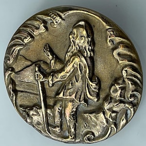 May include: A round, antique brass button with a detailed relief of a bearded figure holding a staff, set against a landscape. The button's edge features an ornate, textured border, and the overall design has a vintage aesthetic.