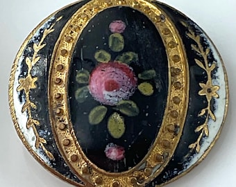 May include: A round button featuring a central black oval panel with a hand-painted pink rose and green leaves. The button is framed by a textured gold-tone border with small raised dots and gold-tone floral vine accents on the black edges.