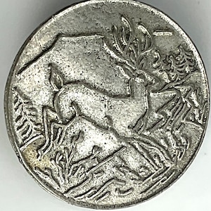 May include: Silver-toned metal coin with a detailed design of two deer in a forest setting. The deer are facing each other, with one deer's antlers raised. The coin has a smooth, slightly textured surface.