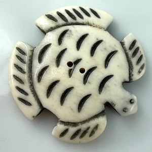 May include: A decorative button in the shape of a fish. The button is off-white with dark brown accents. The fish has two small holes for sewing and is approximately 2 inches wide.