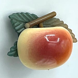 May include: A vintage apple-shaped brooch with a gradient of red and yellow hues. The apple has a brown stem and green leaves. The brooch is likely made of plastic or resin.
