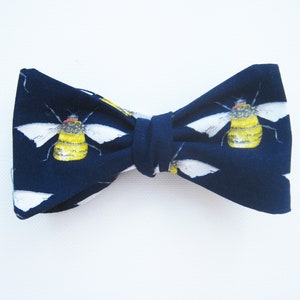 May include: A navy blue bow tie with a white and yellow bee pattern.