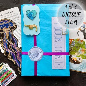 Cita a ciegas con un libro – Caja de regalo edición playa de verano con pins, pegatinas, tarjeta y sorpresas / Regalo misterioso para amantes de los libros con temática oceánica