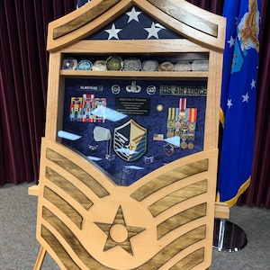 May include: A wooden display case with a star and stripes design, showcasing military medals, coins, and insignia. The case features a blue background and the words "US Air Force" and "Olmstead".