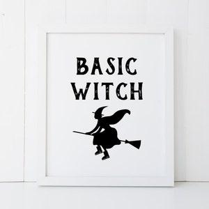 May include: A white framed print with black text that reads "BASIC WITCH" and a silhouette of a witch flying on a broomstick.