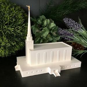 Könnte beinhalten: Weißes 3D-gedrucktes Modell eines Tempels mit einem hohen Turm und einer goldenen Spitze. Das Modell steht auf einem Sockel mit einem kleinen Eingang.